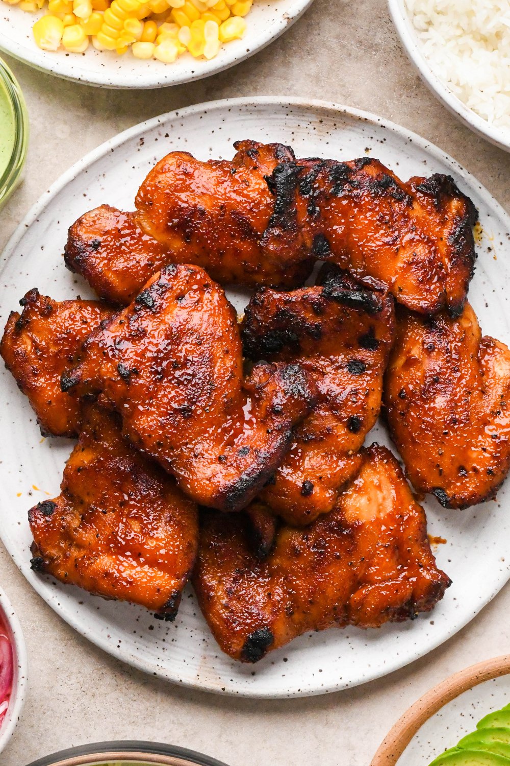 How to make BBQ Chicken Rice Bowls: Crispy caramelized BBQ chicken thighs on a speckled ceramic plate.