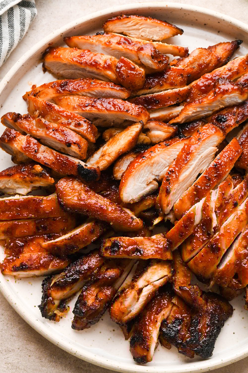 How to make BBQ Chicken Rice Bowls: Cooked BBQ chicken thighs sliced into thin pieces on a speckled ceramic plate.