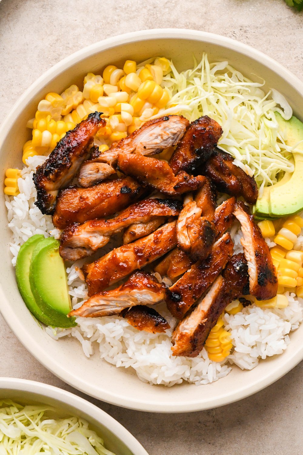 How to make BBQ Chicken Rice Bowls: Rice, shredded cabbage, cooked corn, avocado, and thinly sliced BBQ chicken in a shallow bowl.