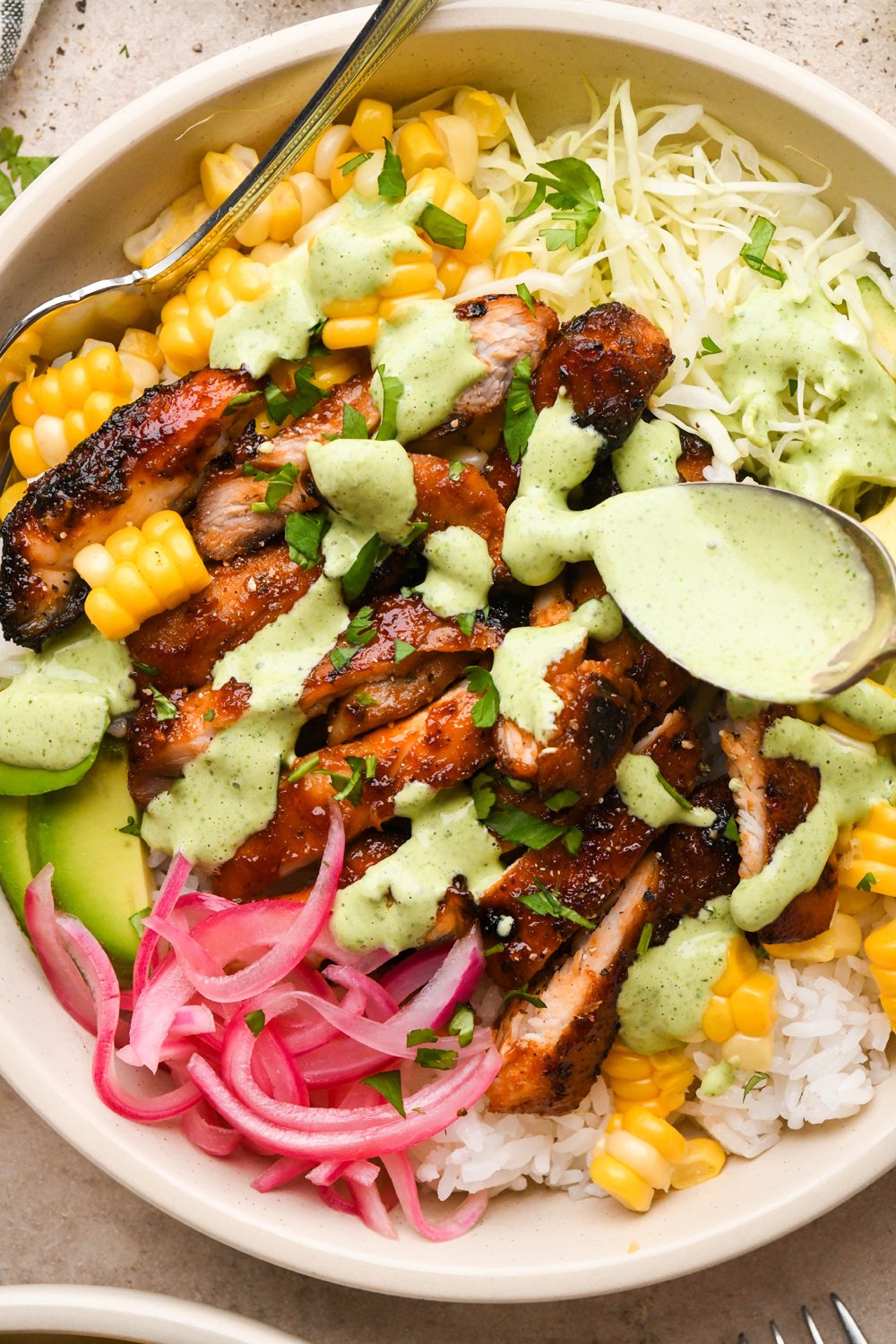 How to make BBQ Chicken Rice Bowls: A spoon drizzling cilantro ranch over BBQ chicken rice bowls.