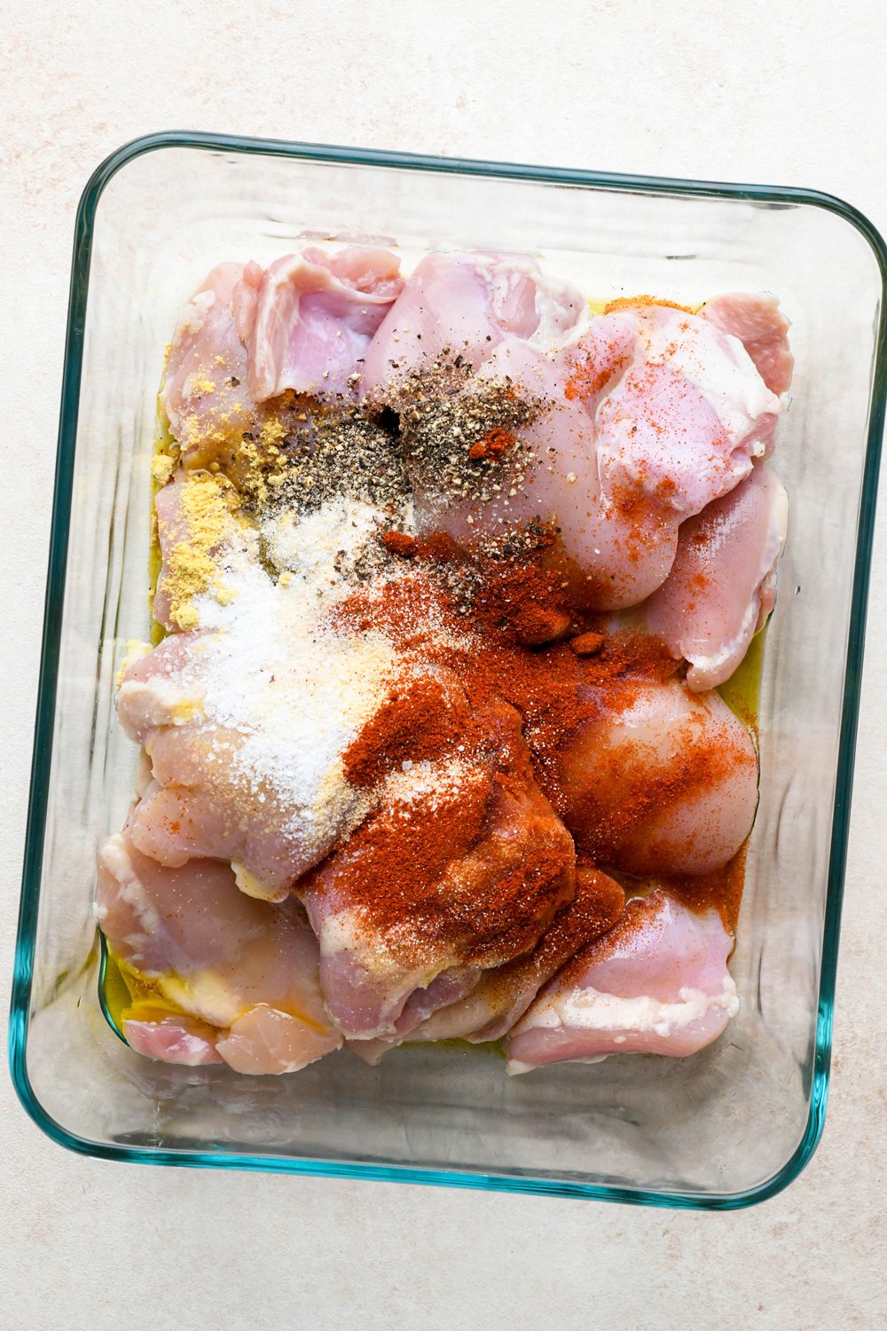 How to make BBQ Chicken Rice Bowls: Chicken thighs in a glass container with spice blend sprinkled on top of the chicken.