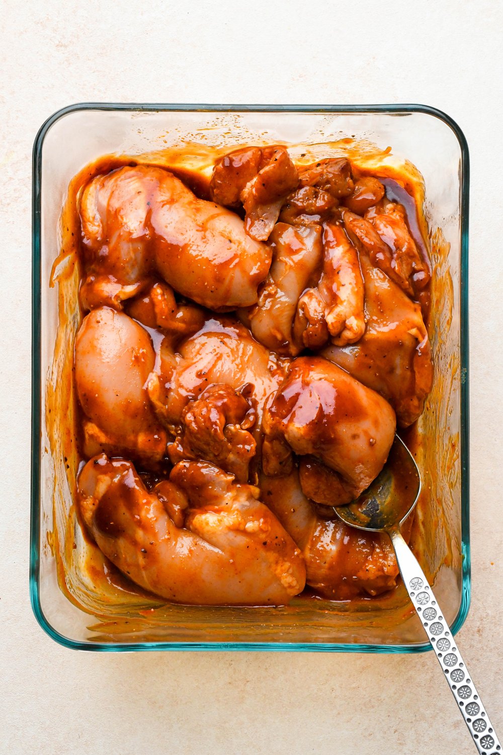 How to make BBQ Chicken Rice Bowls: Chicken thighs in a glass container with spice blend and BBQ sauce. 