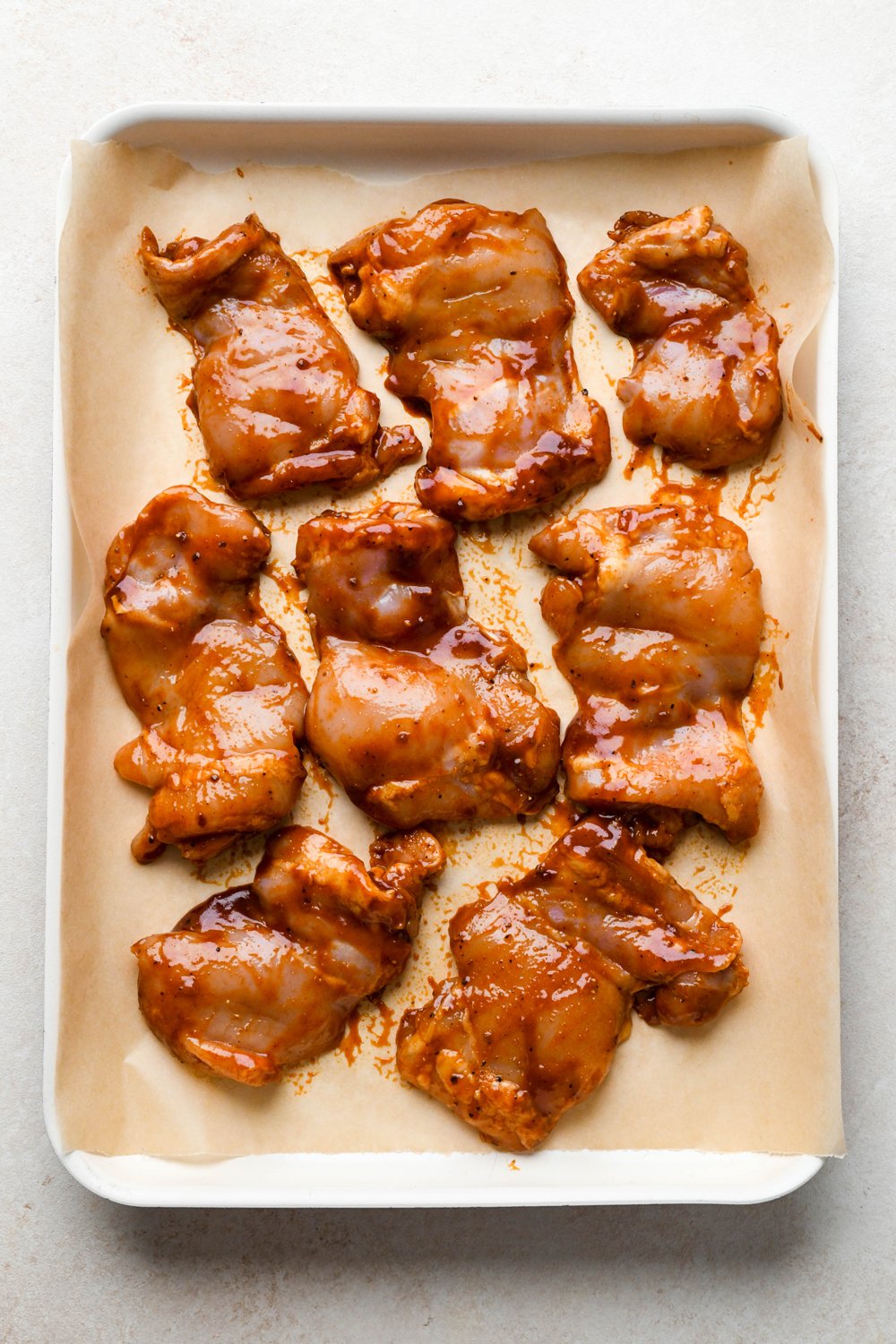 How to make BBQ Chicken Rice Bowls: Marinated chicken thighs on a baking sheet, before cooking.