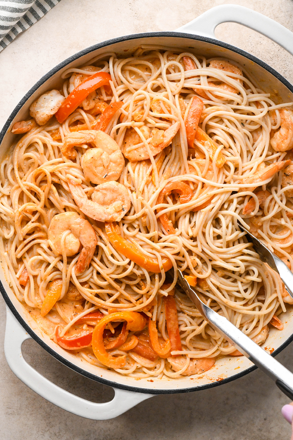 How to make dairy free cajun shrimp pasta step-by-step photos: Tongs tossing pasta together with the sauce.