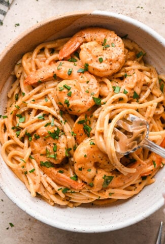 A ceramic bowl of dairy free cajun shrimp pasta, garnished with fresh parsley and black pepper. A fork is digging into the bowl, twirling a bite of pasta and lifting it up to show the creamy texture of the sauce.