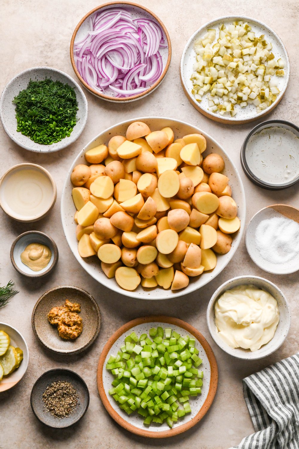Ingredients to make Dill Pickle Potato Salad with Creamy Dill Dressing in various ceramics on a light creamy brown backdrop. 