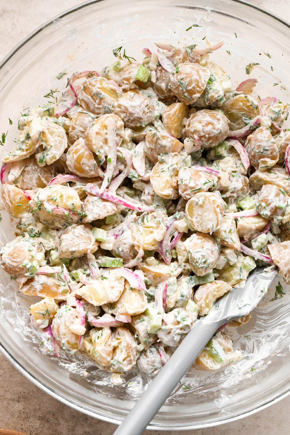 How to make Dill Pickle Potato Salad with Creamy Dill Dressing: Mayonnaise, chopped pickles, diced celery, and fresh herbs added to the large glass mixing bowl with potatoes, after stirring to combine.