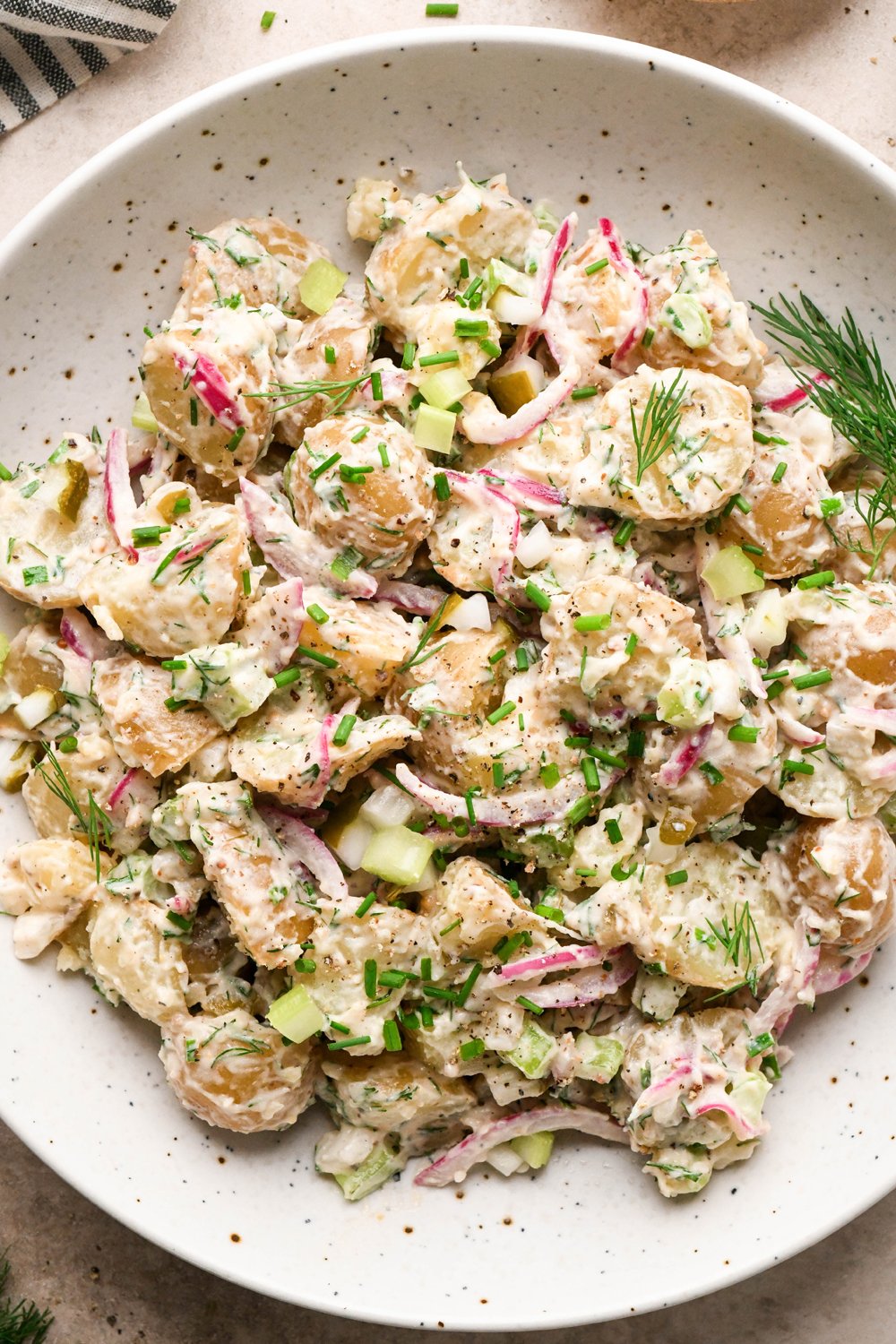 A large shallow speckled bowl filled with creamy mayo-based dill pickle potato salad. 