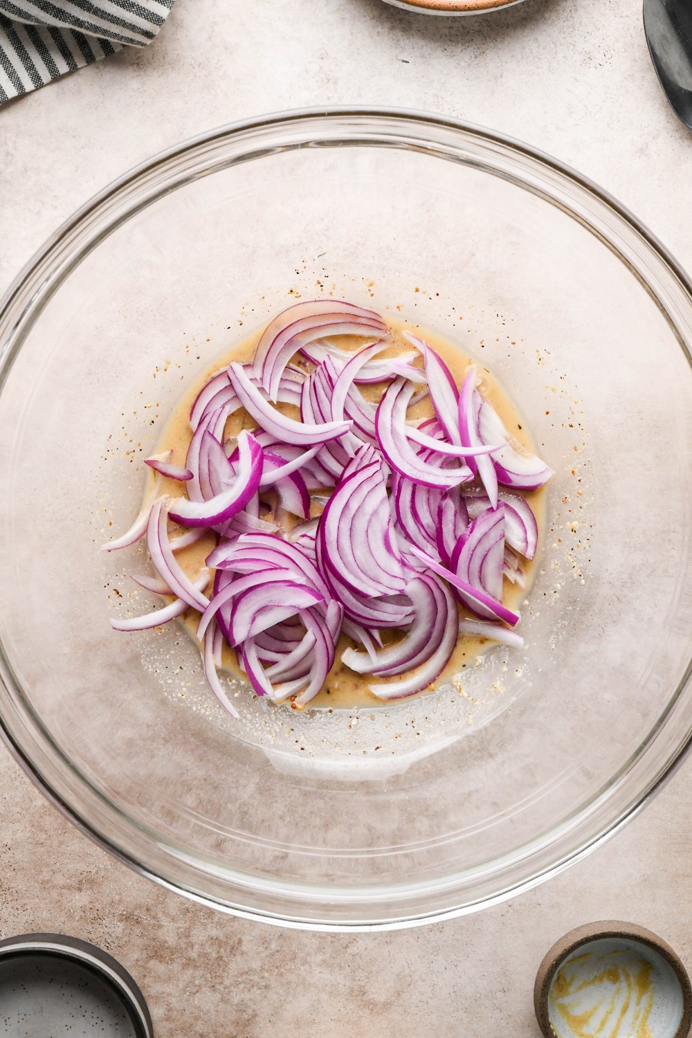 How to make Dill Pickle Potato Salad with Creamy Dill Dressing: Thinly sliced raw red onion added to the large glass bowl with mustard, vinegar, and pickle brine mixture.