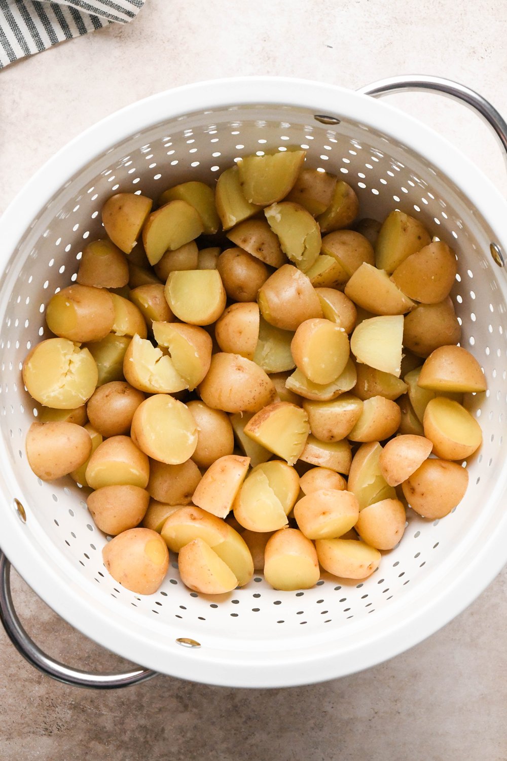 How to make Dill Pickle Potato Salad with Creamy Dill Dressing: Cooked baby potatoes drained in a large white strainer.