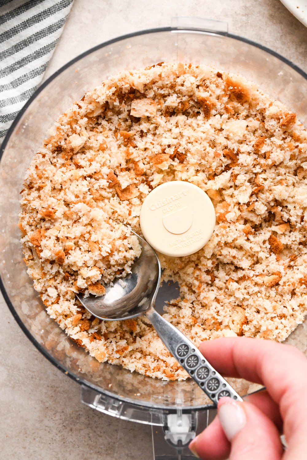How to make a Caesar Salad with gluten free breadcrumbs: A spoon lifting out a portion of the pulsed breadcrumbs from the food processor container to show the texture. 