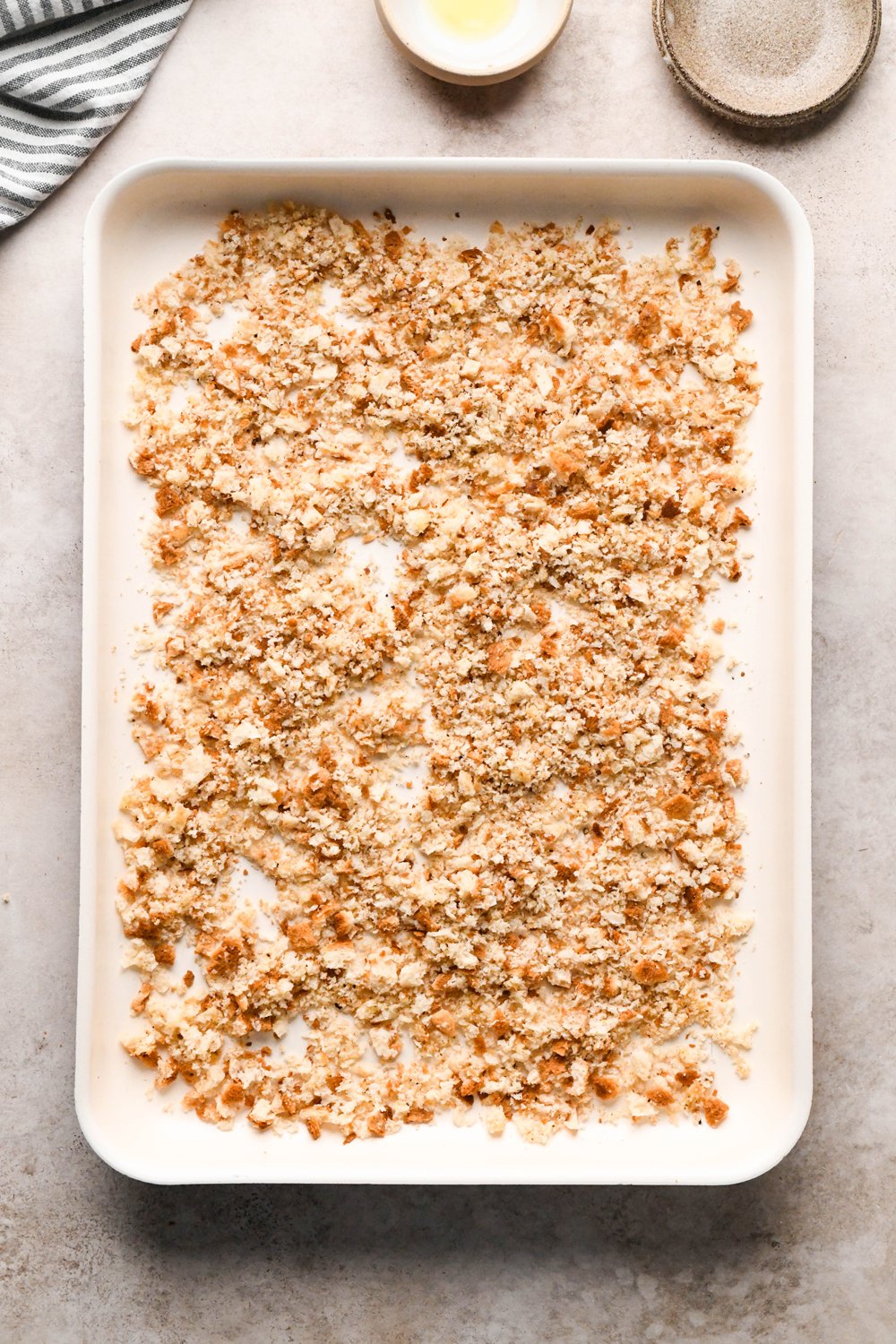 How to make a Caesar Salad with gluten free breadcrumbs: Breadcrumbs on a baking sheet spread out evenly after being tossed with the olive oil, salt, pepper, and garlic powder.