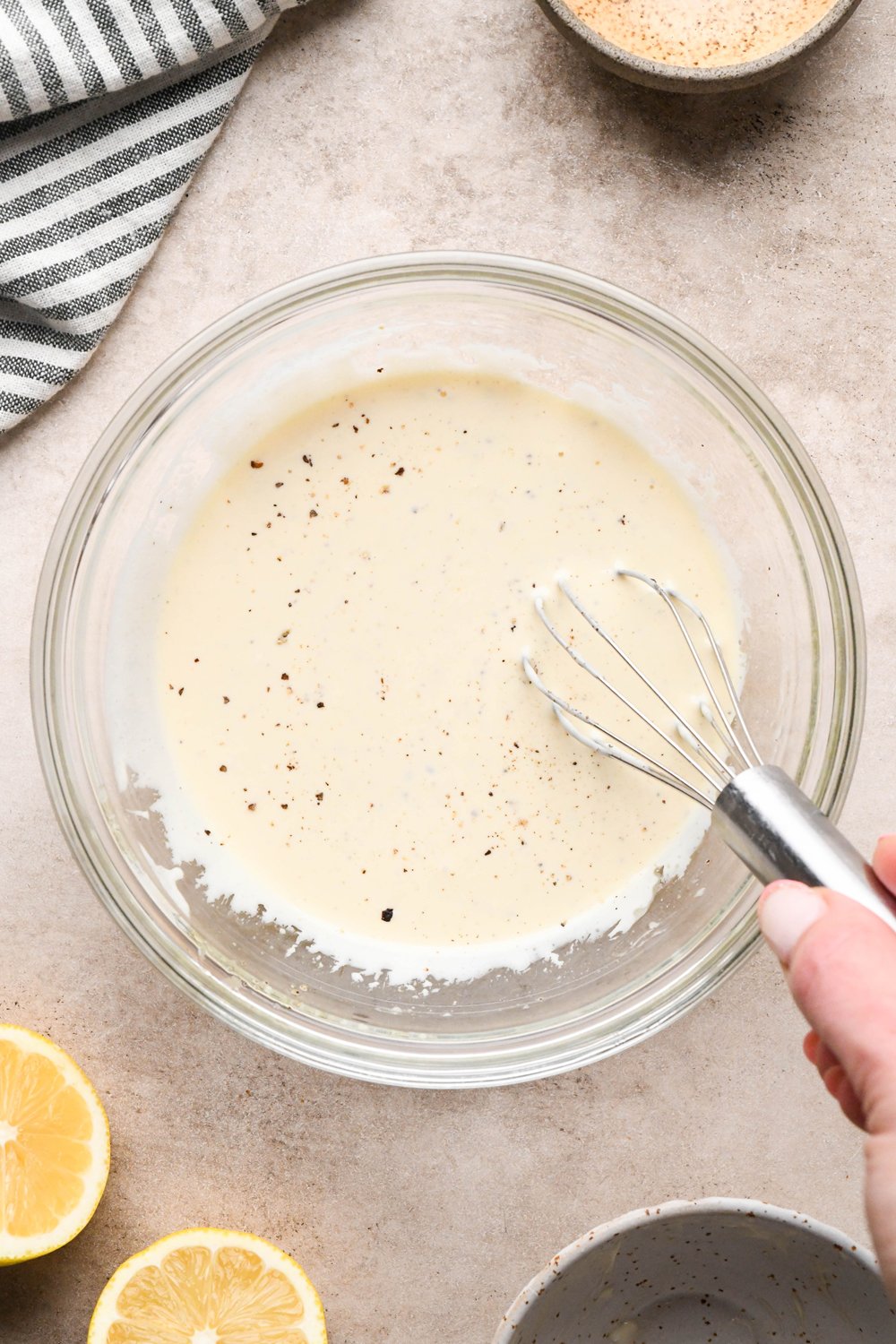 How to make a Caesar Salad with gluten free breadcrumbs: Caesar salad dressing whisked together in a small glass bowl with visible flecks of black pepper. 