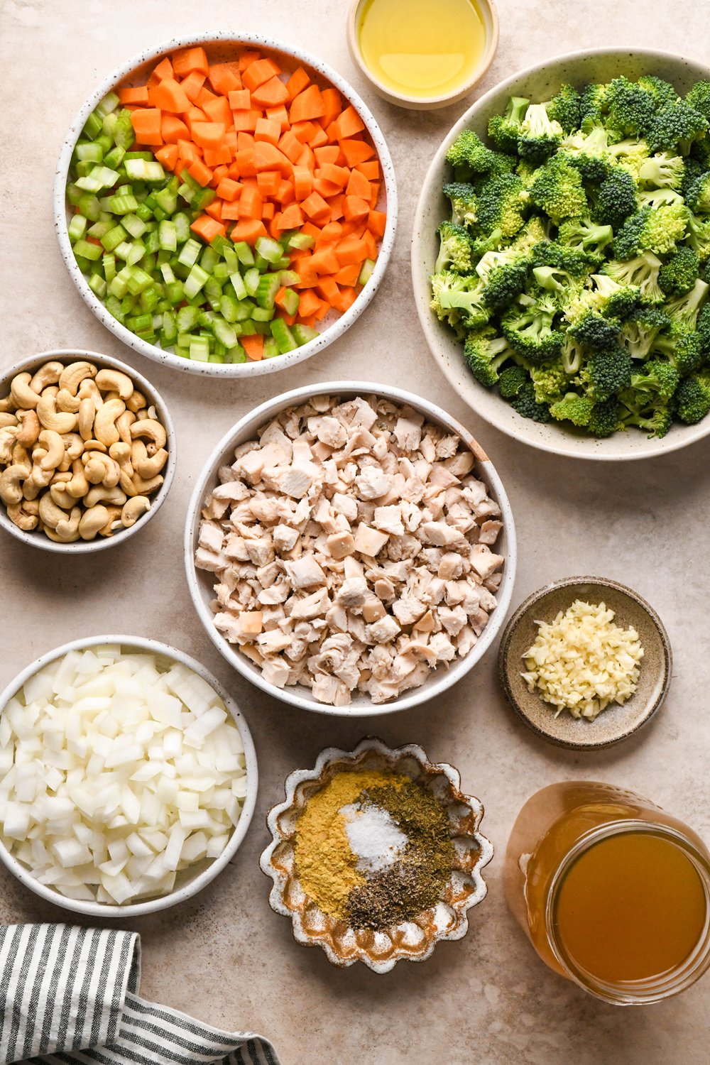 Ingredients for chicken and broccoli soup in various ceramics on a light creamy brown background.