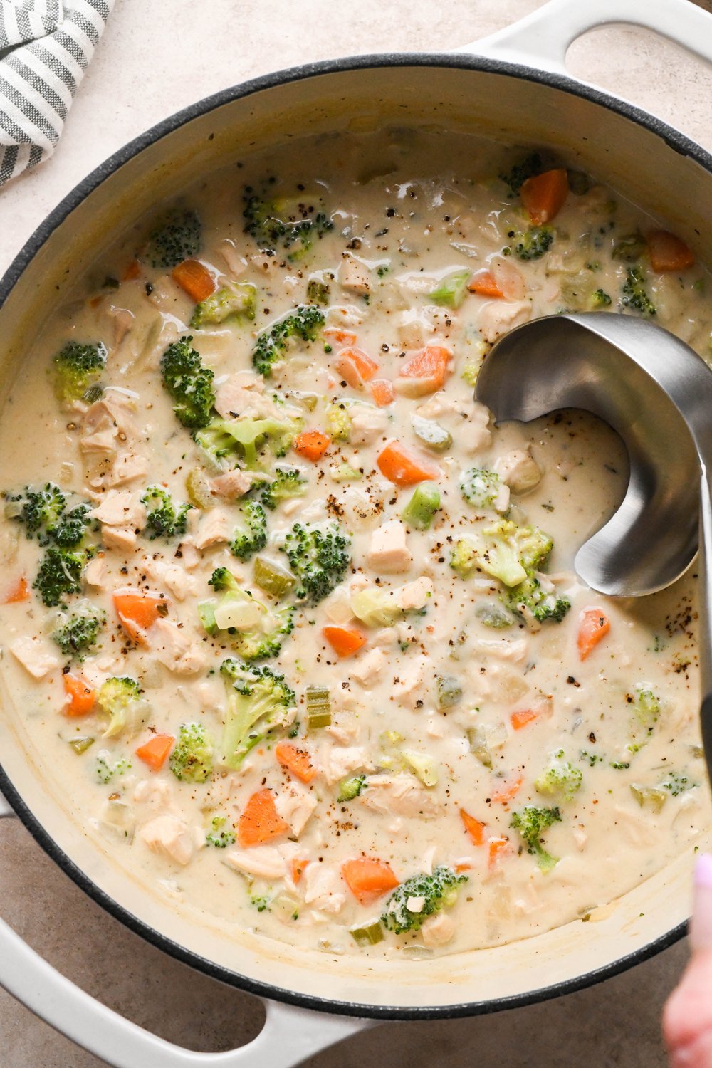 A large white ceramic coated soup pot of creamy dairy free chicken and broccoli soup, with lots of broccoli florets. A ladle is dipping into the soup to lift out a portion for serving.
