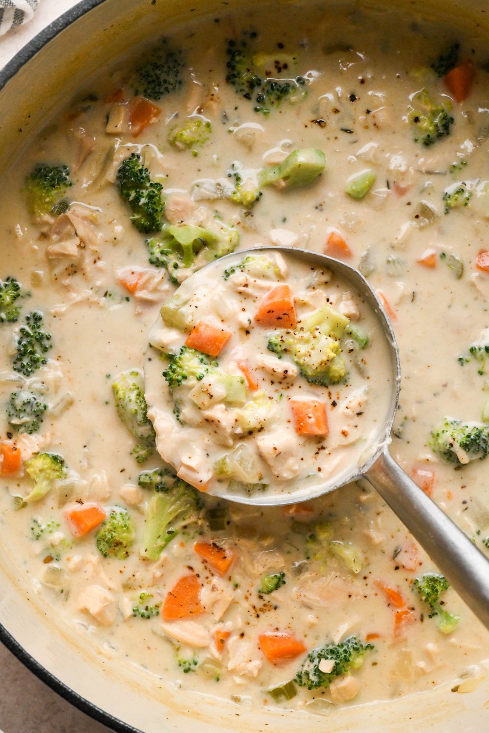 A large white ceramic coated soup pot of creamy dairy free chicken and broccoli soup, with lots of broccoli florets. A ladle is dipping into the soup to lift out a portion for serving.