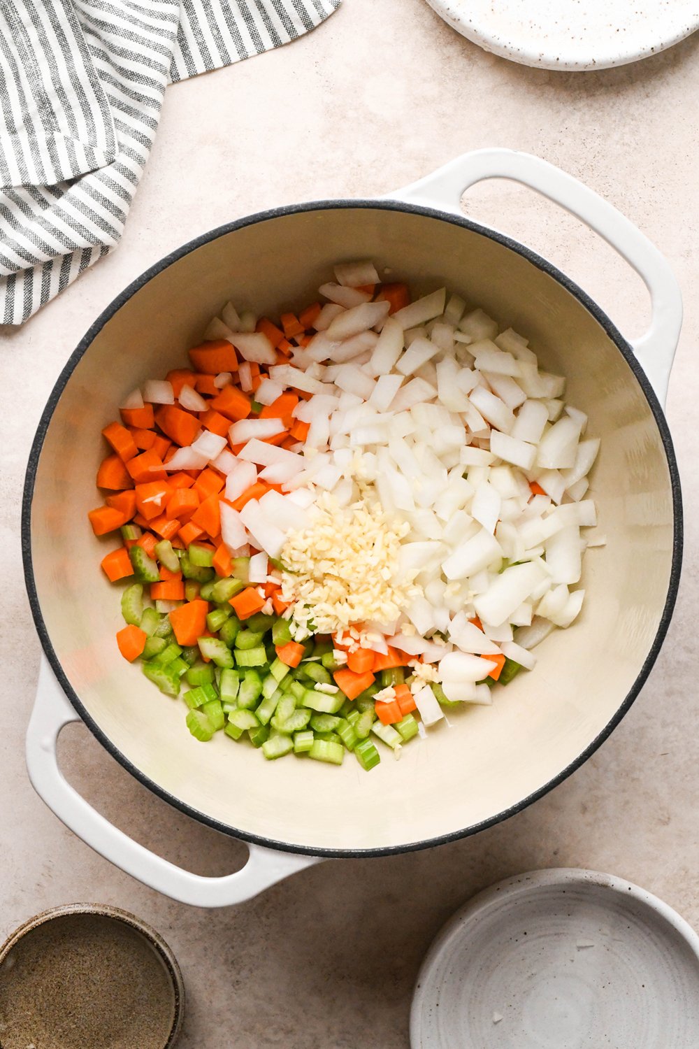How to make Chicken and Broccoli Soup: Diced carrots, diced celery, diced onion, and chopped garlic in a large off-white ceramic soup pot with olive oil, before sautéing. 