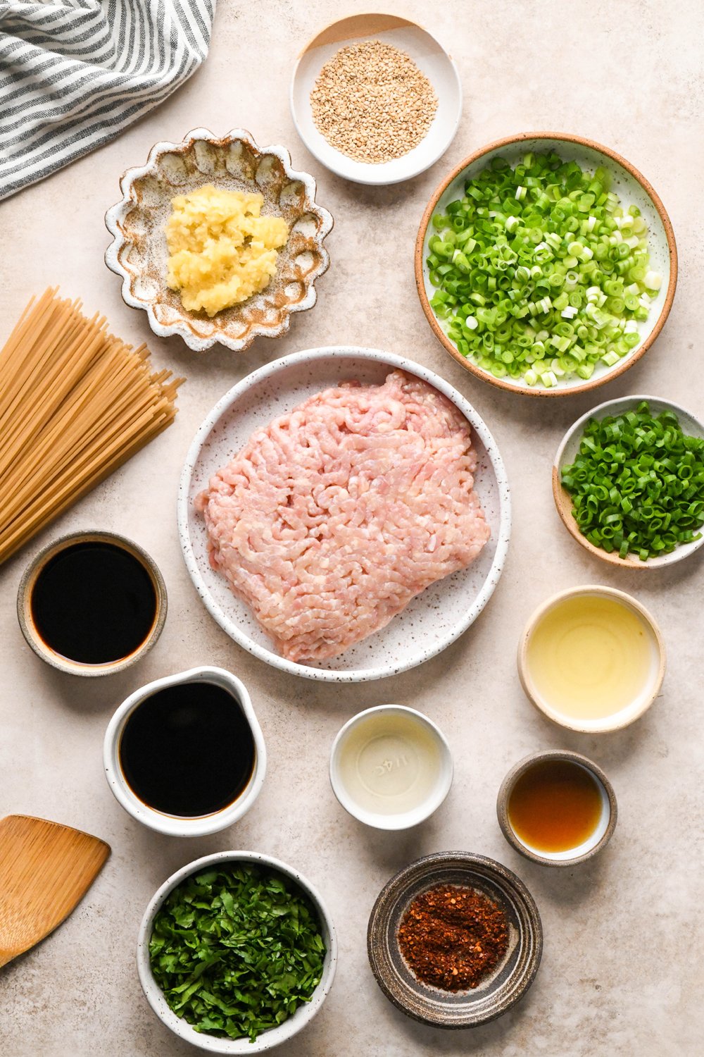 Ingredients for garlic scallion noodles in various ceramics on a creamy brown background.