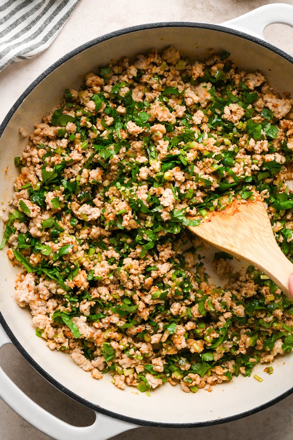 How to make garlic scallion noodles: A wooden spatula stirring the cilantro and sesame seeds into the ground chicken.
