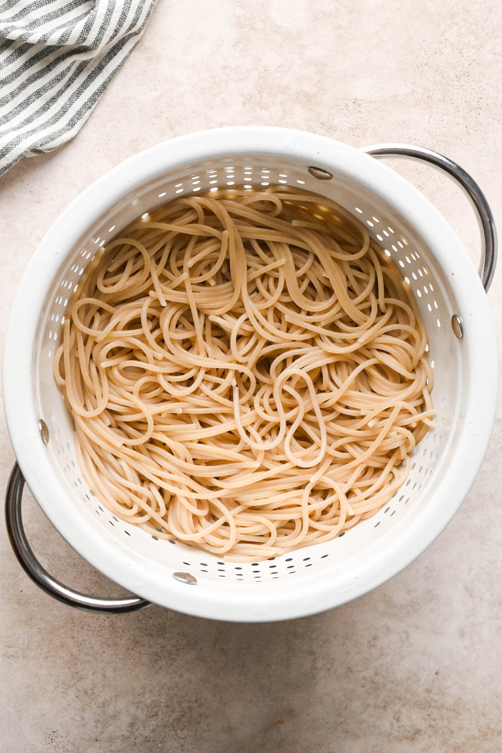 How to make garlic scallion noodles: Cooked gluten free spaghetti noodles drained in a white colander.
