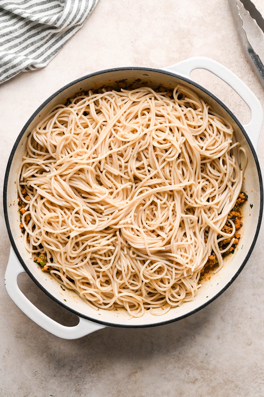 How to make garlic scallion noodles: Cooked gluten free spaghetti noodles added to the skillet with the ground chicken sauce, before tossing to combine.