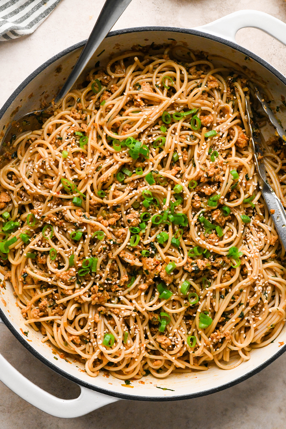 How to make garlic scallion noodles: Cooked gluten free spaghetti noodles added to the skillet with the ground chicken sauce, after tossing to combine, garnished with green onions and more sesame seeds.