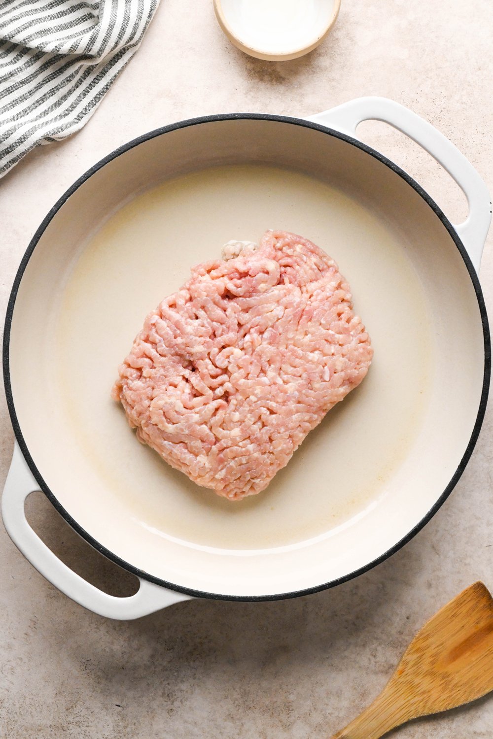 How to make garlic scallion noodles: Raw ground chicken in a large cream colored enamled skillet.