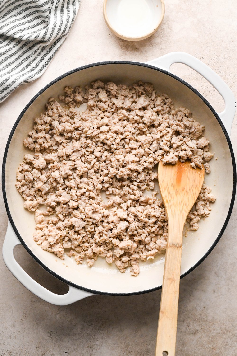 How to make garlic scallion noodles: Ground chicken broken apart and cooked in a cream colored enameled skillet.
