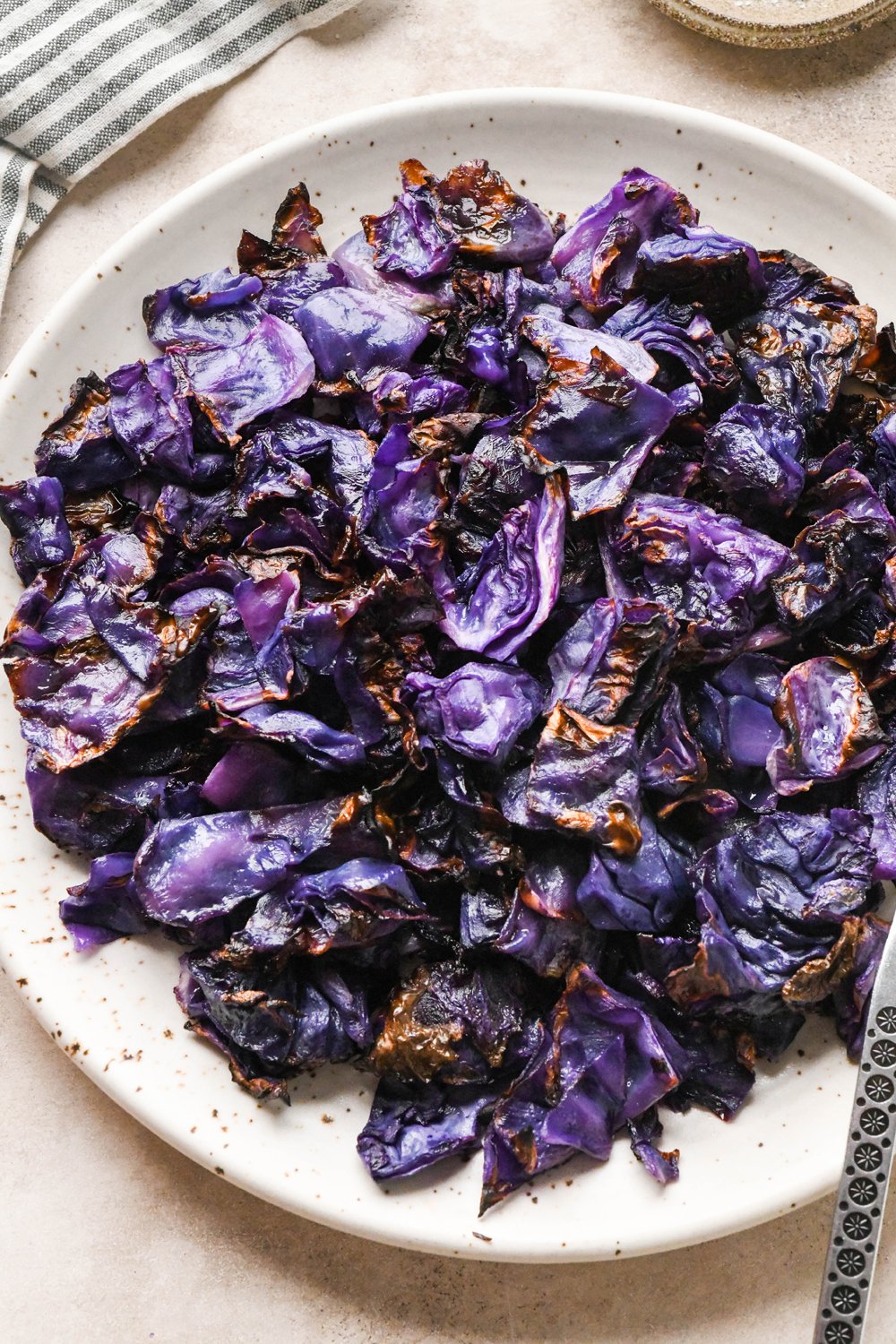 Pieces of roasted red cabbage on a large speckled plate, with a metal serving spoon angled onto the plate for serving.