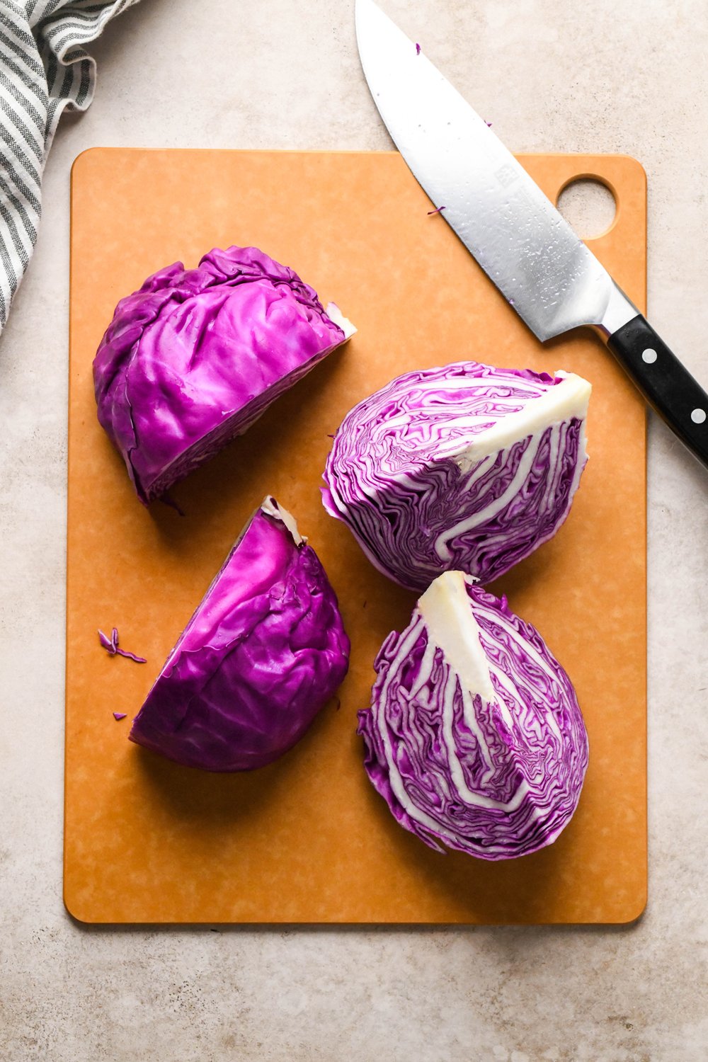 How to make Roasted Chopped Red Cabbage with Olive Oil: A medium sized head of red cabbage is on a cutting board next to a knife, after having been cut into quarters.