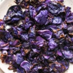 Pieces of roasted red cabbage on a large speckled plate, with a metal serving spoon angled onto the plate for serving.