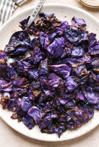 Pieces of roasted red cabbage on a large speckled plate, with a metal serving spoon angled onto the plate for serving.