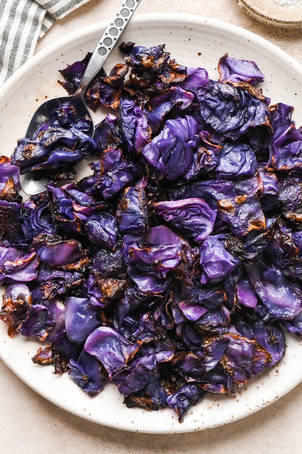 Pieces of roasted red cabbage on a large speckled plate, with a metal serving spoon angled onto the plate for serving.