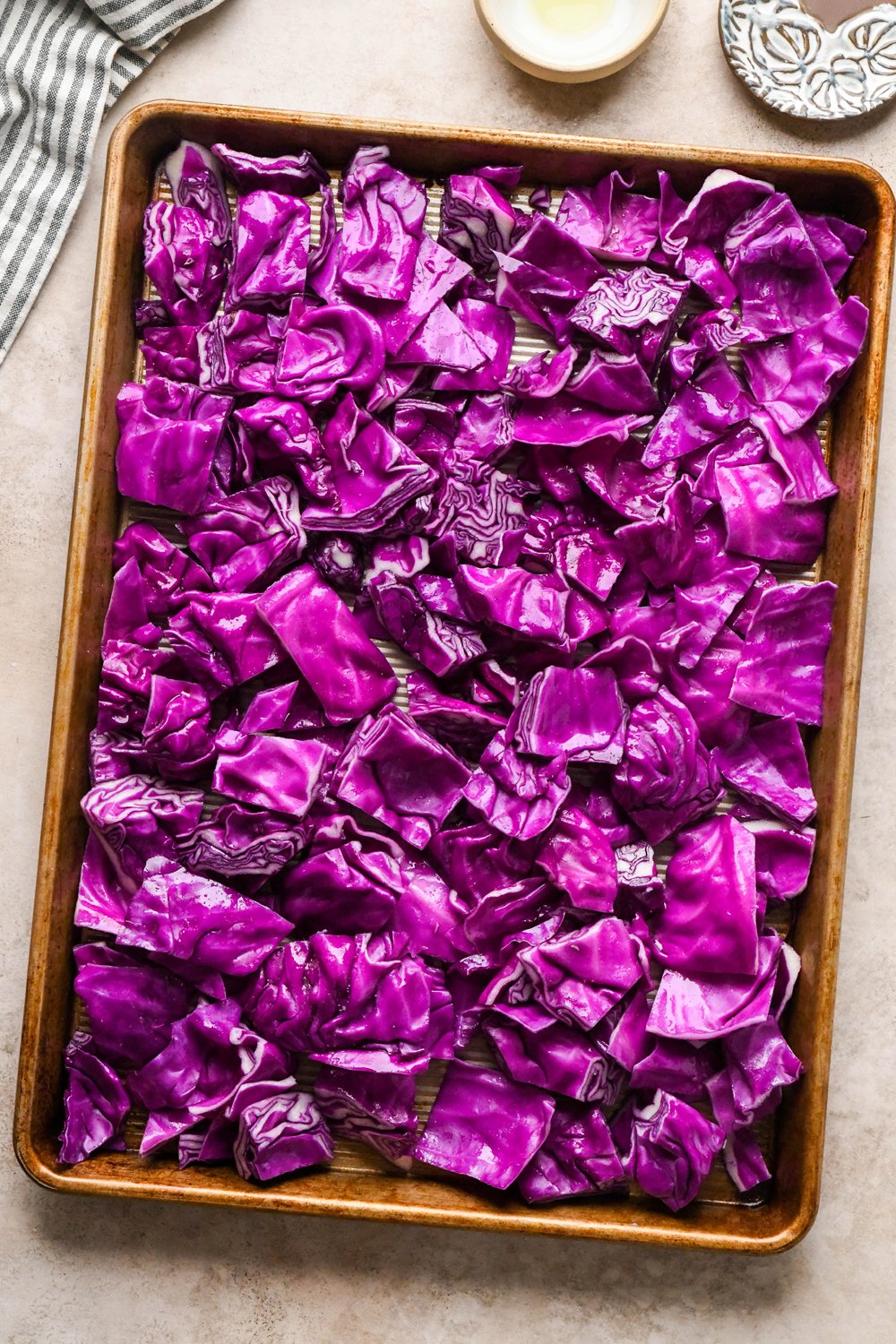 How to make Roasted Chopped Red Cabbage with Olive Oil: Cut red cabbage pieces have been tossed with olive oil and salt and are spread out evenly on a large metal rimmed baking sheet.