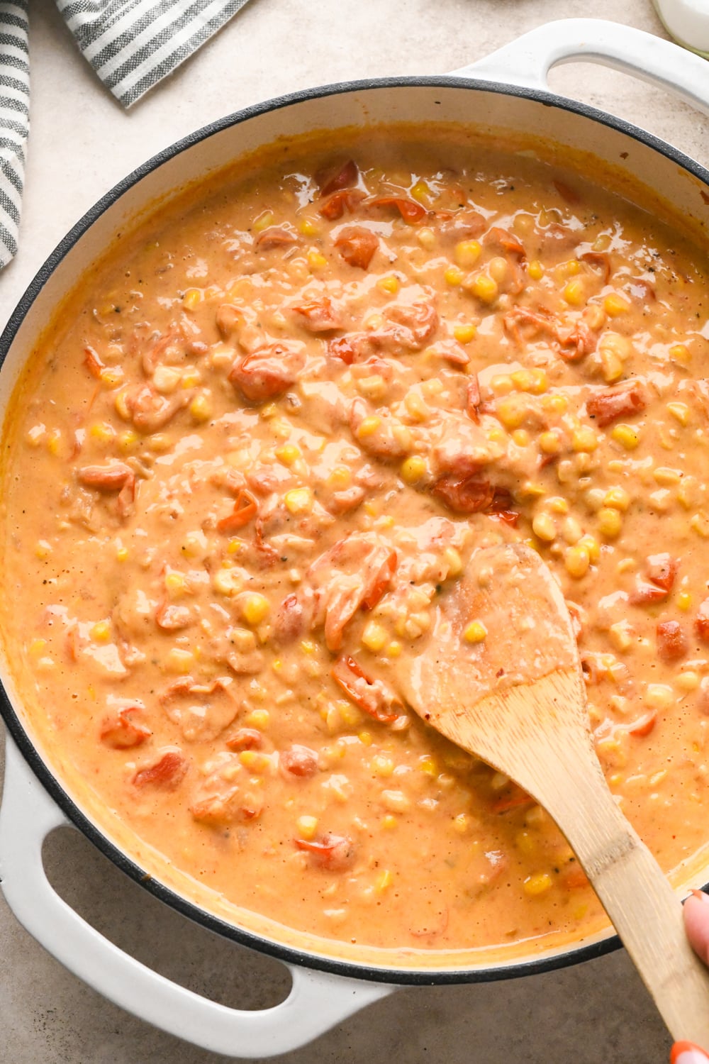 A wooden spoon stirring the cashew cream, cherry tomato, and corn sauce to show the robust and creamy texture.