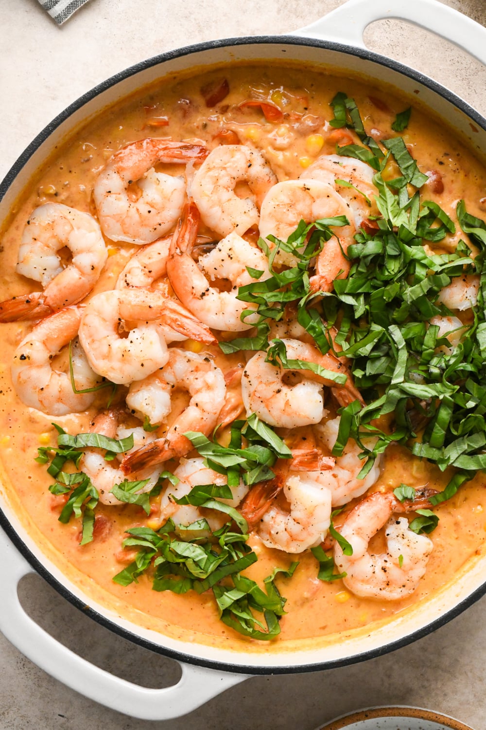Shrimp and fresh basil added to the sauce before stirring to combine in a large white skillet on a light surface.