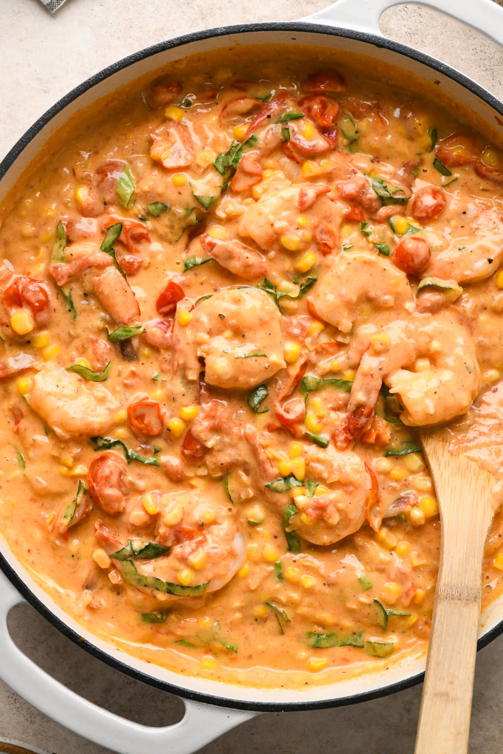 Shrimp and fresh basil added to the sauce after stirring to combine in a large white skillet on a light surface.