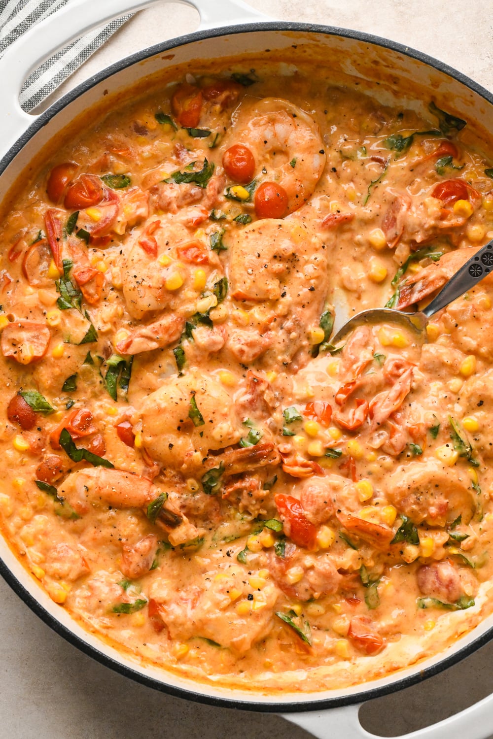 Creamy skillet dish with shrimp, cherry tomatoes, and corn, mixed in a rich, orange-colored cashew cream sauce. A spoon is partially dipped in, ready to serve.