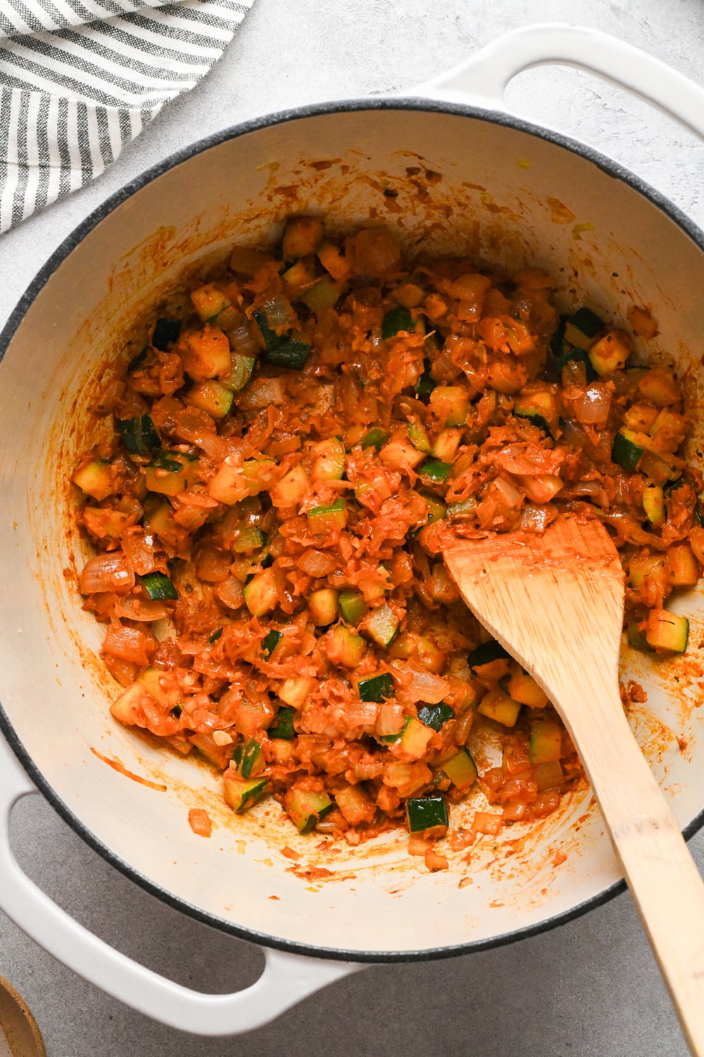 Tomato paste and spices stirred into the zucchini and aromatics after cooking for a few minutes in a large white soup pot.