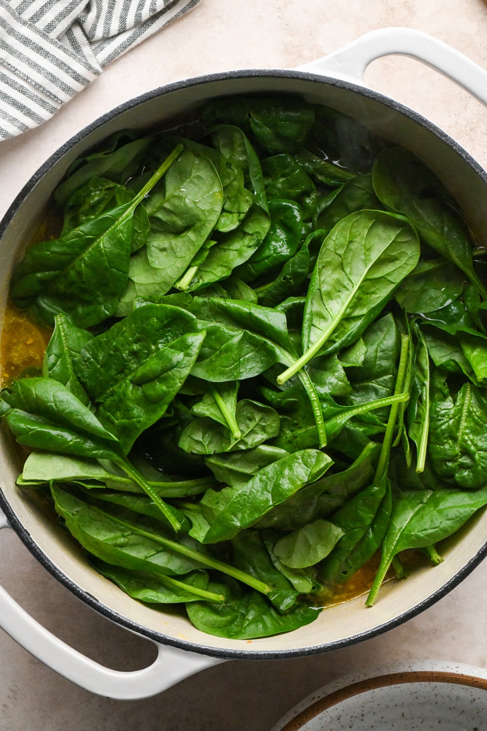 Baby spinach added to the soup in a large white dutch oven.