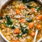 A bowl of Italian sausage soup containing ground Italian sausage, pasta stars, carrots, celery, and spinach.