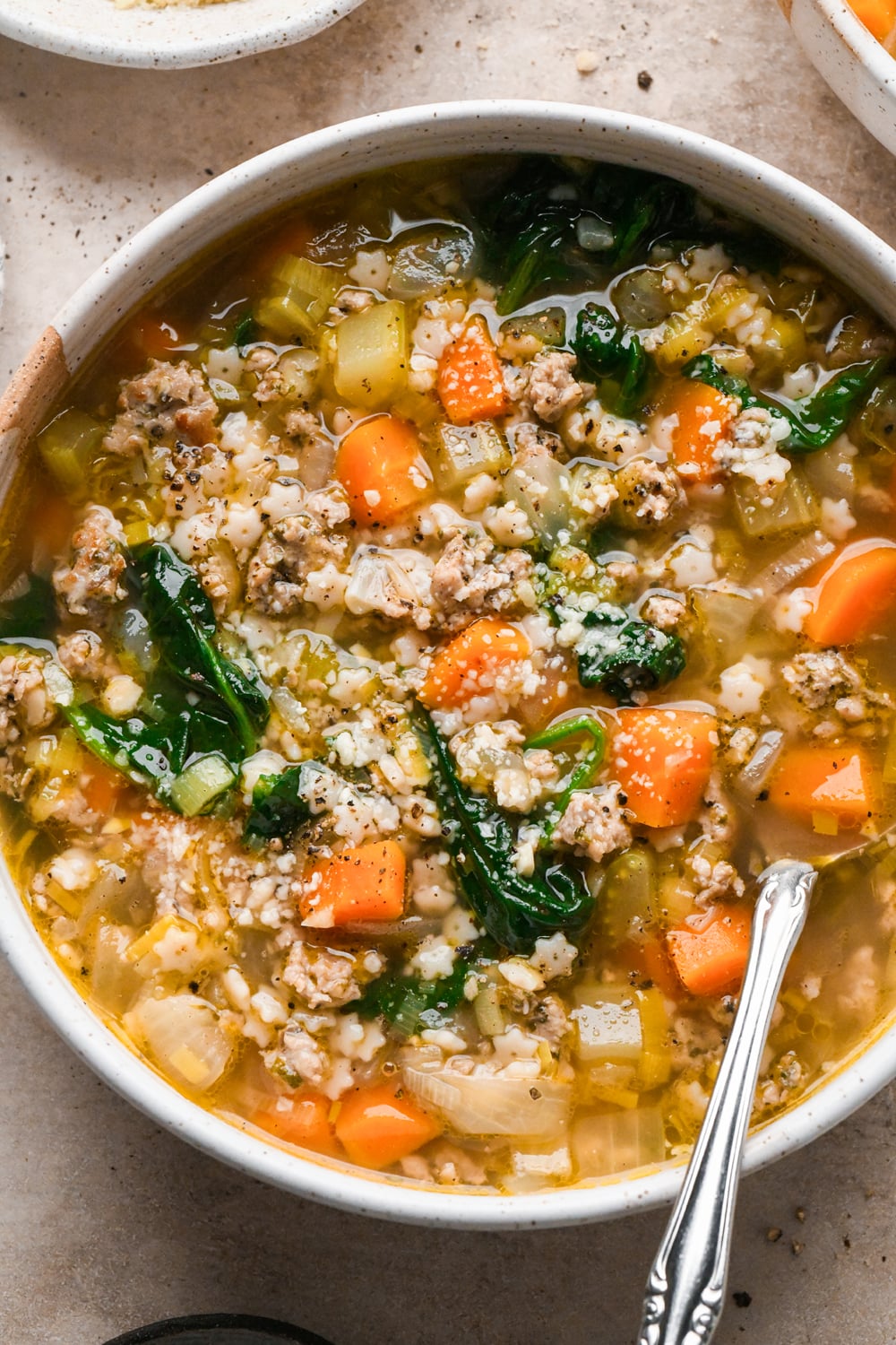 A bowl of Italian sausage soup containing ground Italian sausage, pasta stars, carrots, celery, and spinach.