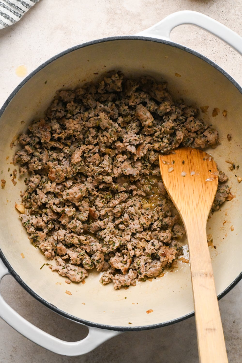 Italian sausage, cooked and crumbled in a large white enameled dutch oven.