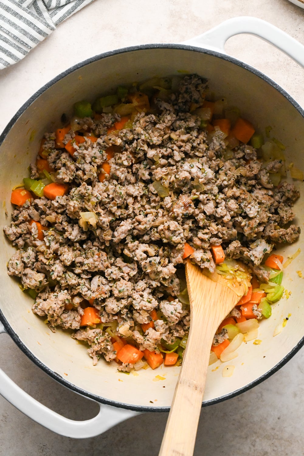 Cooked Italian sausage added to a large enamled white cast iron pot with sautéed vegetables.
