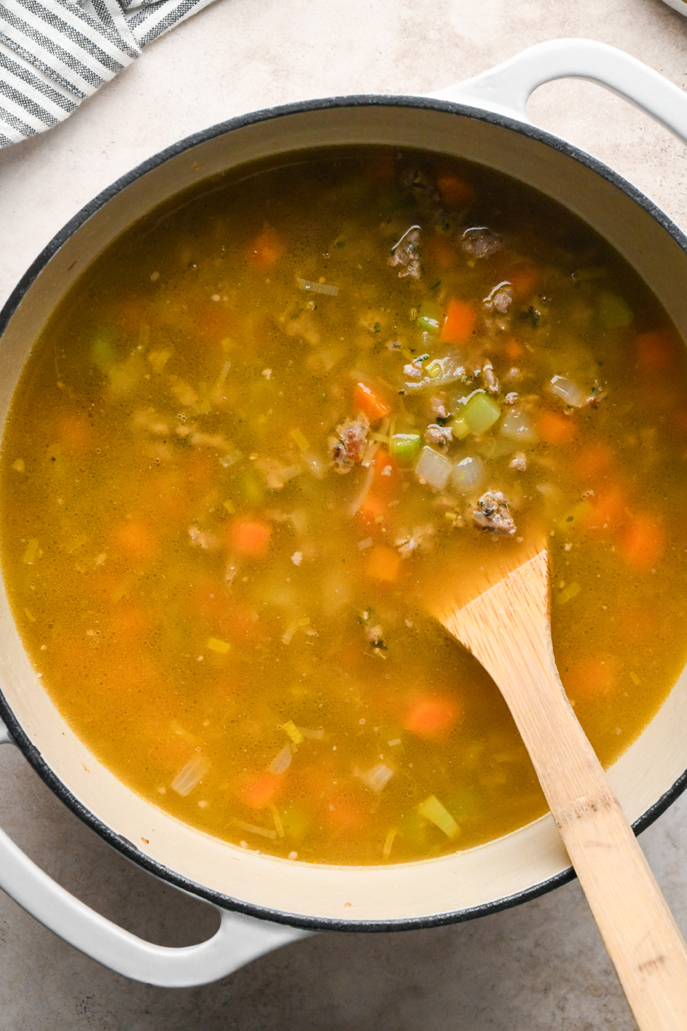 Chicken broth with other soup ingredients in a large white enameled dutch oven, before simmering.