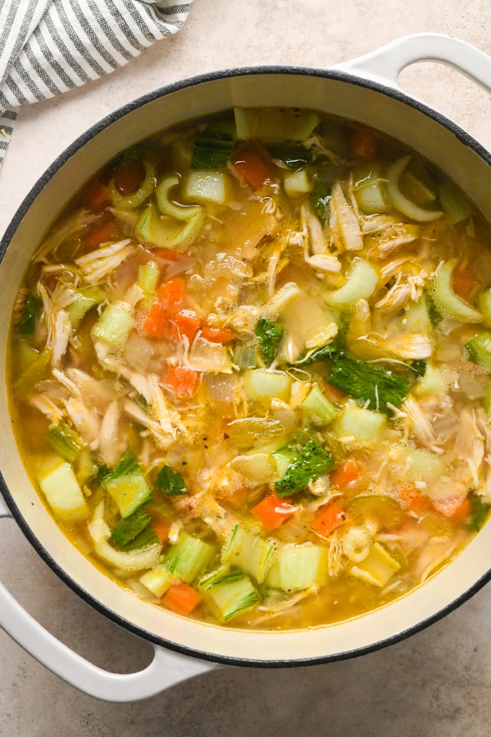 A pot of chicken noodle soup with chopped bok choy and carrots after simmering, with a wooden spoon resting inside.
