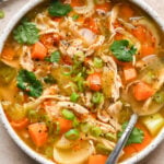 A bowl of ginger chicken soup with carrots, celery, green onions, and cilantro, served with a lime wedge.