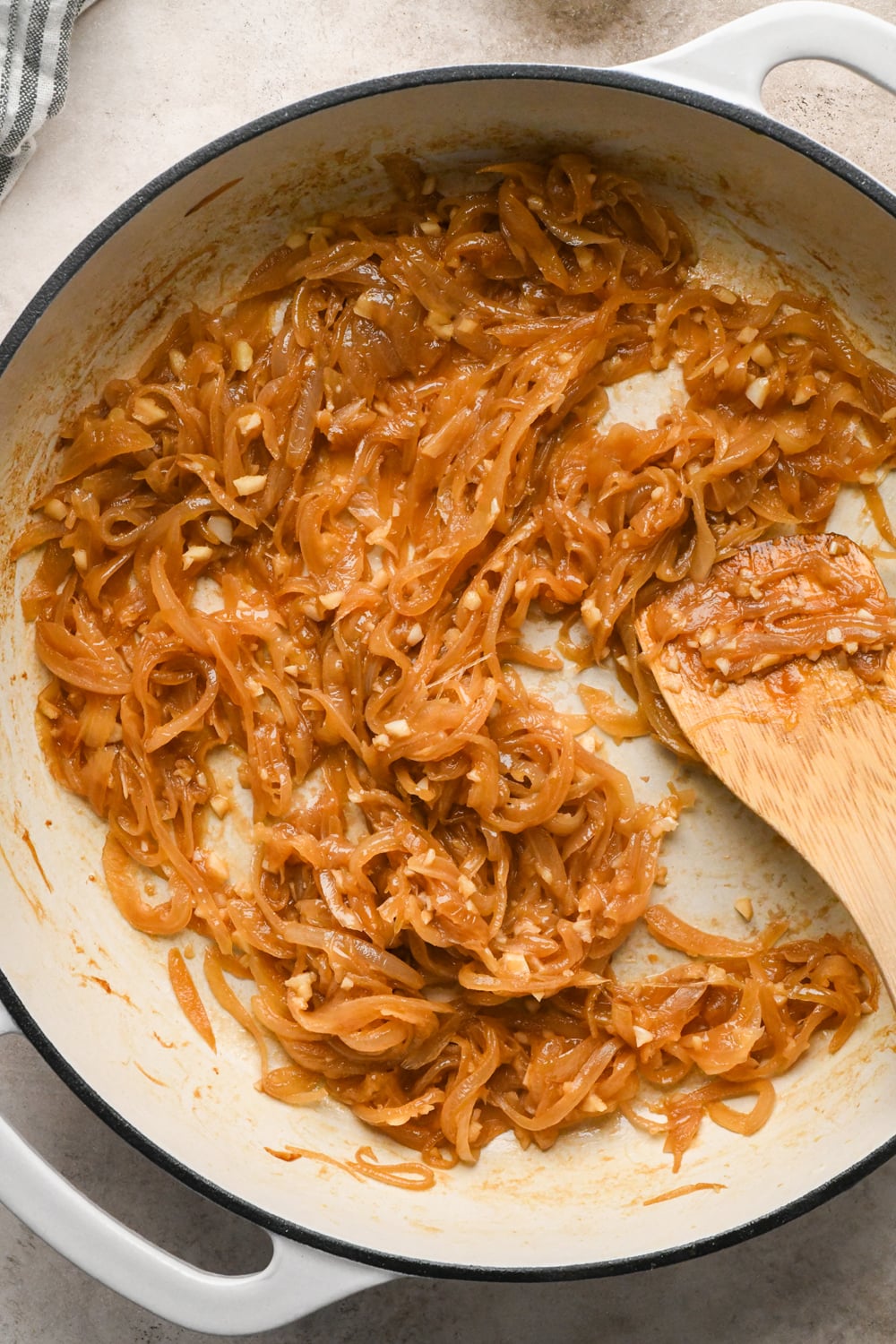 Deeply caramelized sliced white onions with cooked garlic in a white cast iron skillet.