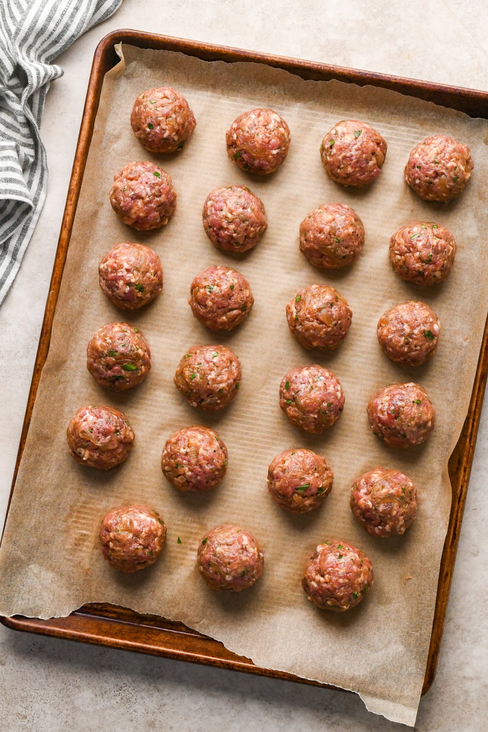 Twenty three raw meatballs arranged in rows on a parchment-lined baking sheet.