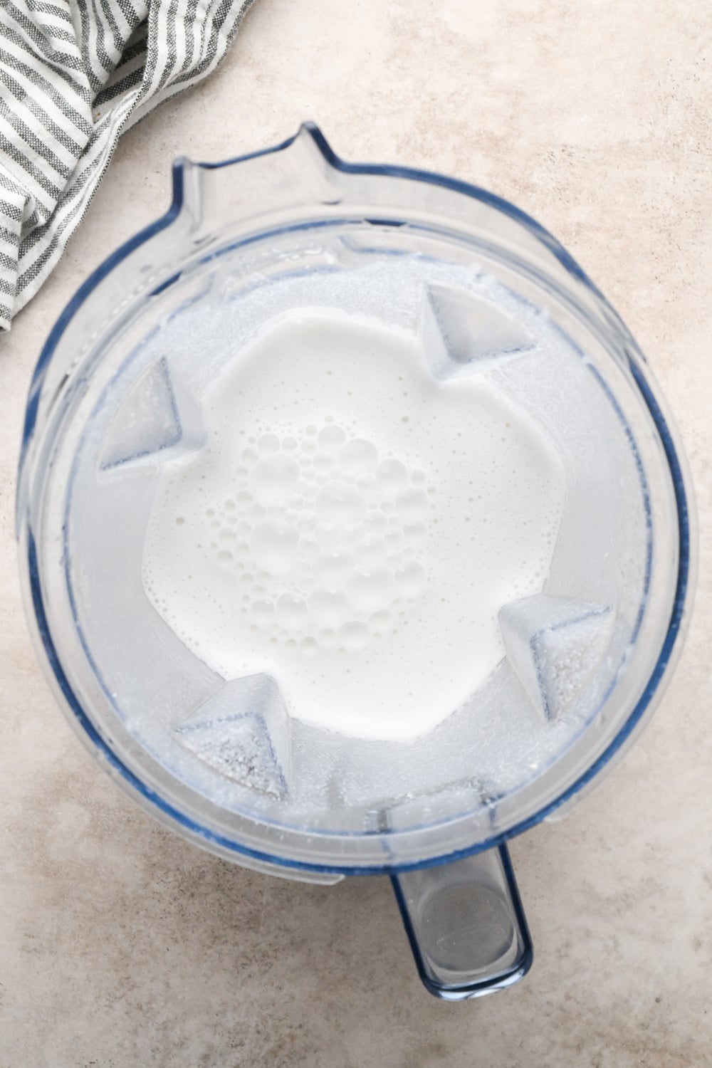 Chicken broth and soaked raw cashews in a Vitamix blender container after blending to create a creamy white sauce.